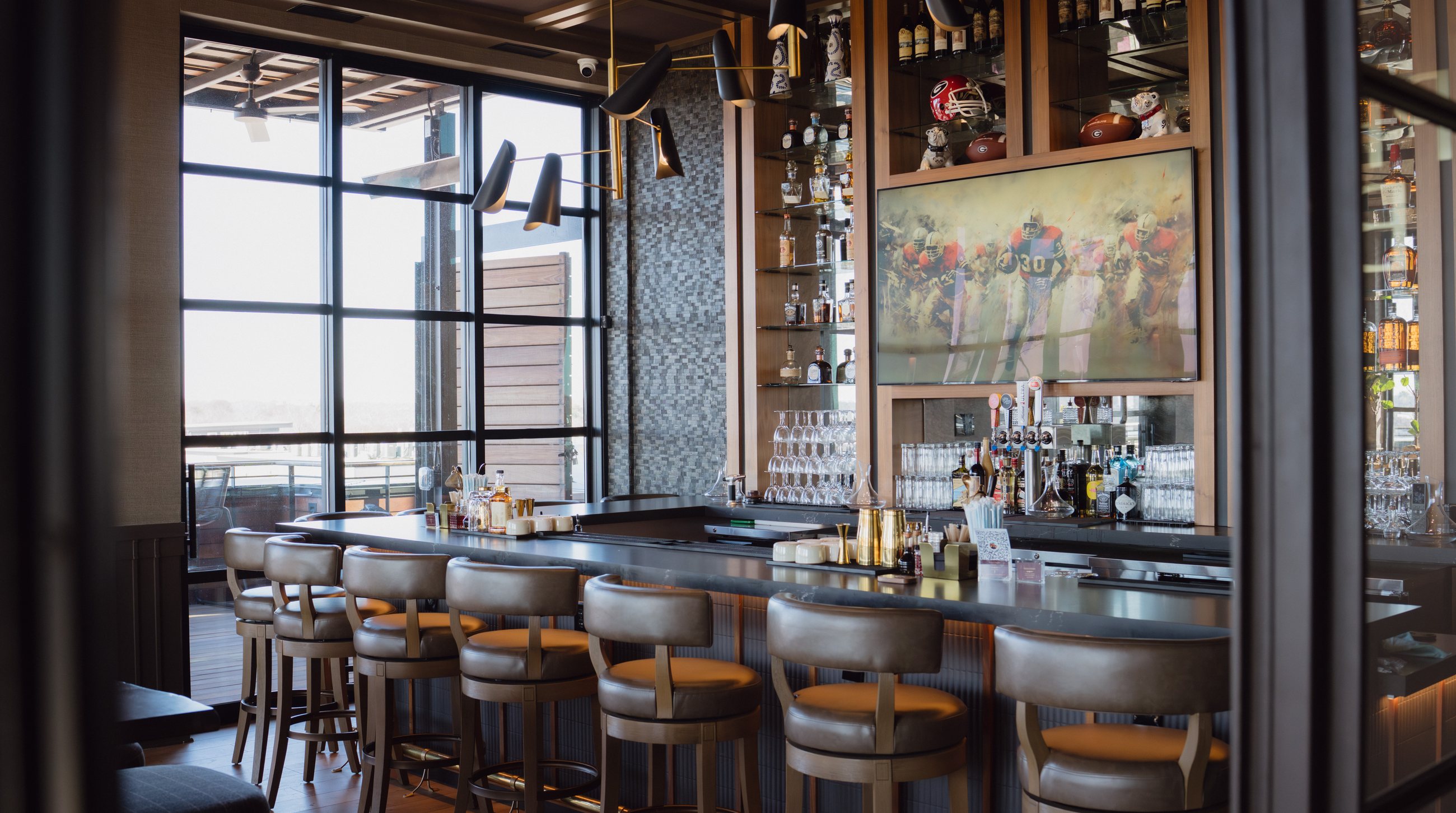 A rooftop members' bar with an art-mode display, backlit spirits, sculptural pendant lighting, and a city view — by Partner Technology