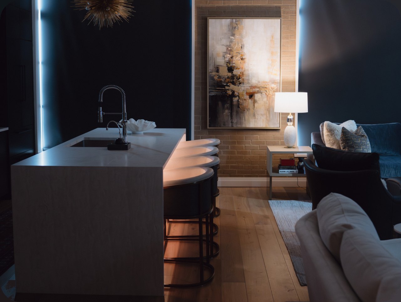 A kitchen island and open living space at night, shaped by warm layered lighting and cove accents